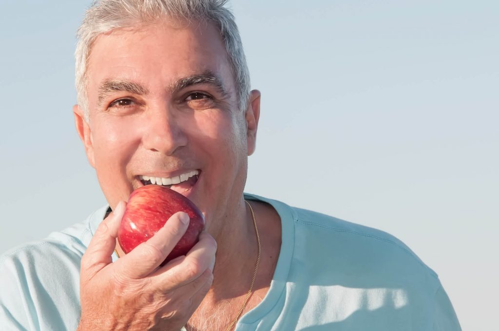 Man with dental implants in Plantation biting an apple